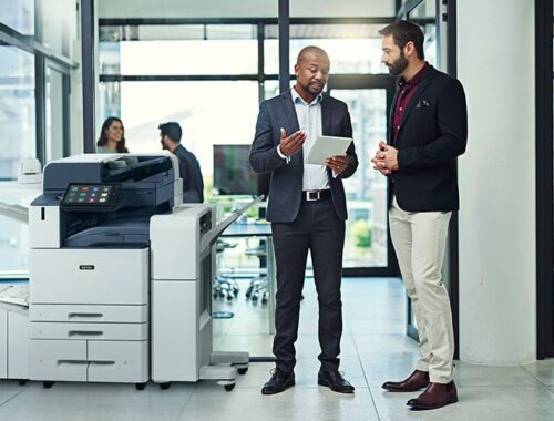 Deux hommes dans un bureau discutent sur une tablette à côté d'une imprimante multifonction couleur Xerox® AltaLink® série C8200